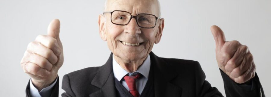 positive senior man in eyeglasses showing thumbs up and looking at camera