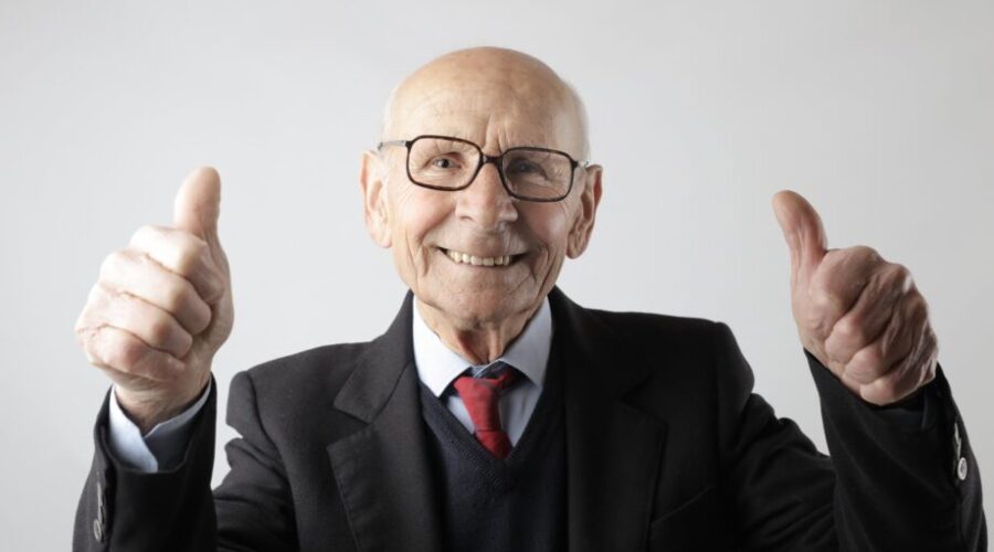 positive senior man in eyeglasses showing thumbs up and looking at camera