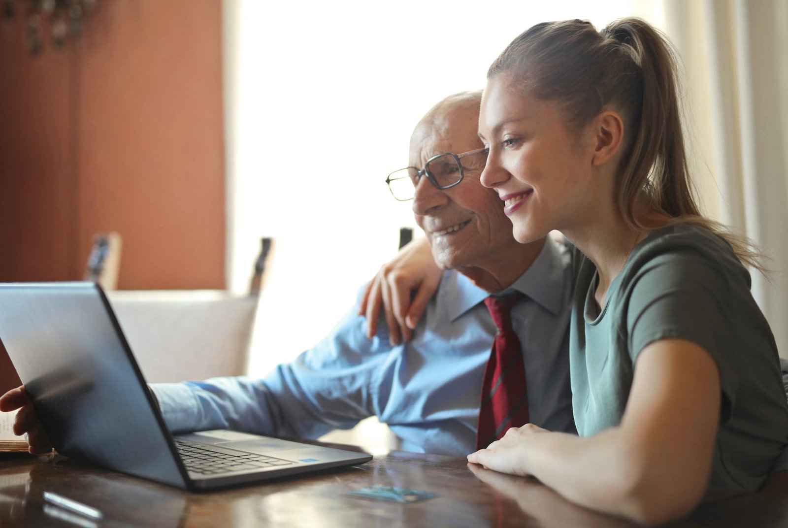 young positive woman helping senior man using laptop