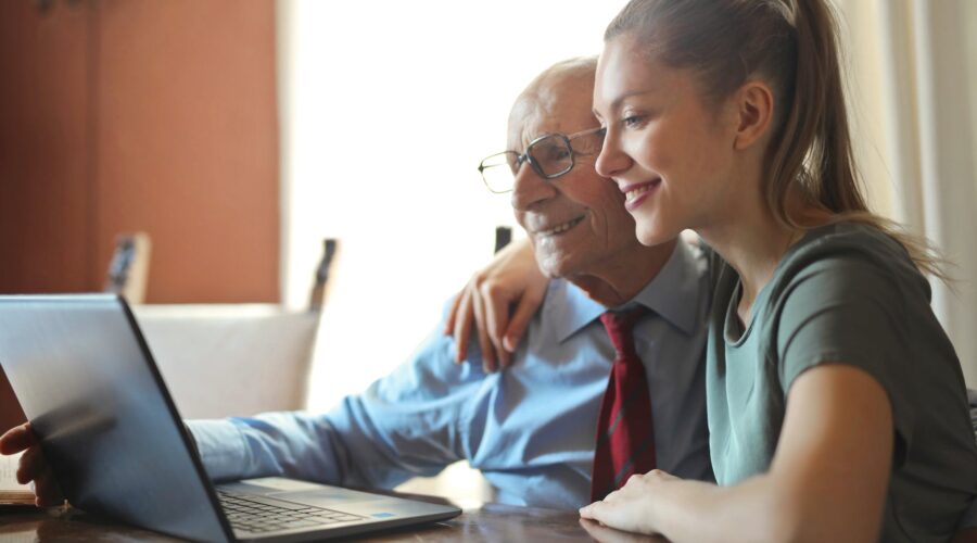 young positive woman helping senior man using laptop