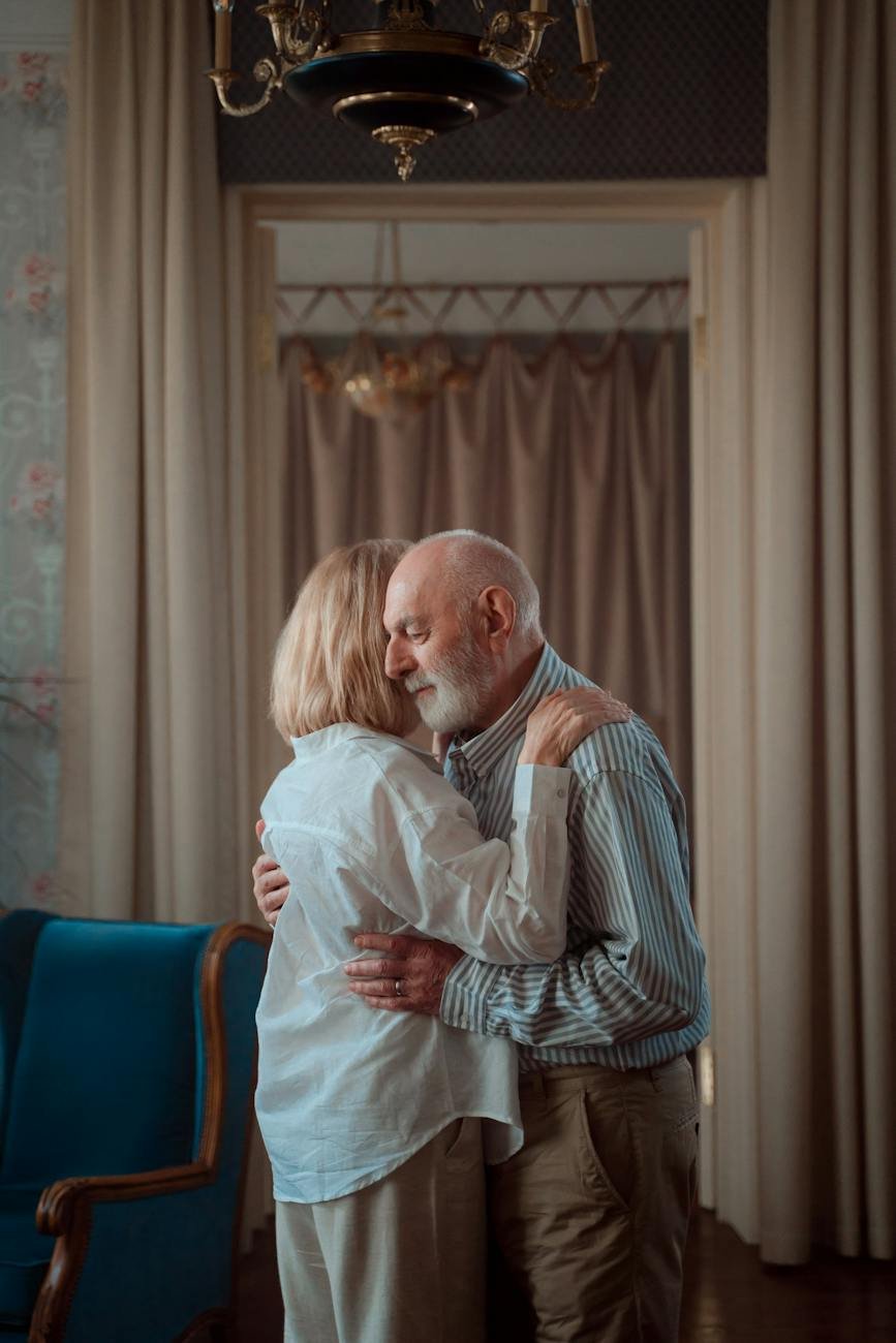 elderly couple standing in a room and hugging